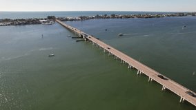 Drone clip over large river with cars driving over long bridge and open sea in the background, on a warm summer day