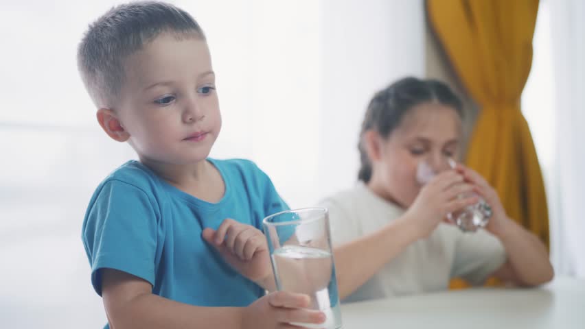 Children indoors drinking glassware water. Crisis clean a drinking water. children in kitchen drink clean water. baby boy drinking water from glass close-up. Little children lifestyle drink