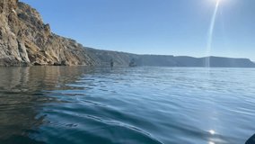 A serene video of sea bay rocks with a kayak on a warm summer day, with the calm azure sea and blue sky creating a tranquil atmosphere.