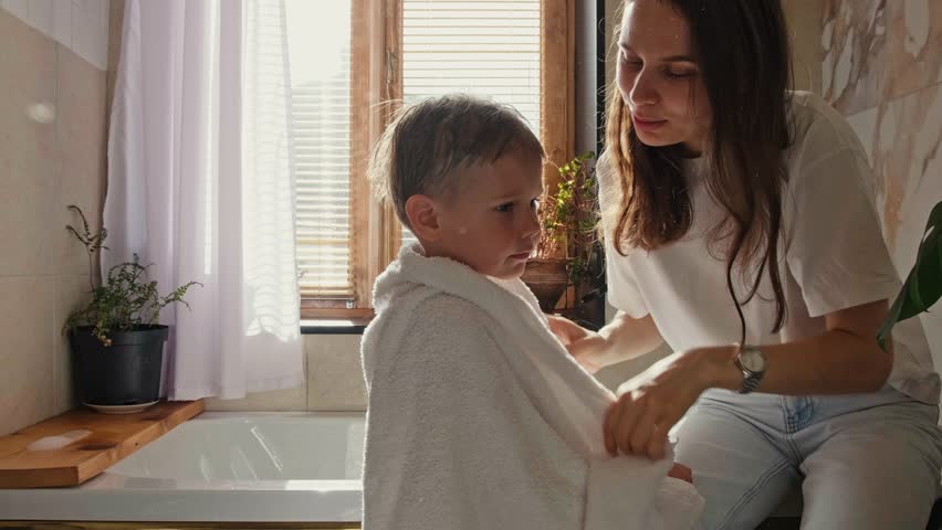 A young mother wipes her son with a towel after a shower. Mom takes care of her son. Morning shower with baby. Royalty-Free Stock Footage #1103174739