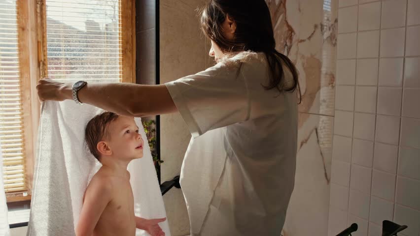A young mother wipes her son with a towel after a shower. Mom takes care of her son. Morning shower with baby. Royalty-Free Stock Footage #1103174743