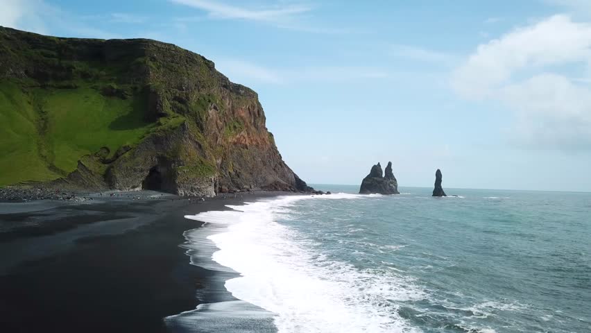 Aerial drone footage of Pointy rocks sticking out of the ocean at Reynisfjara Beach near Vik in Iceland. Pointy Rock cliffs at black sand beach. Basalt cave with basalt column. High quality 4k footage Royalty-Free Stock Footage #1103182667