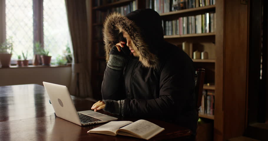 Stressed man wearing a coat inside his house looking at the increasing energy bills.