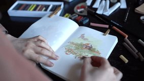 Close up of female artist painting with soft pastels in sketchbook, woman creating pastel painting in studio, sitting at wooden table with art supplies, expressing creativity in drawing - Powered by Shutterstock - Get 15% off with code: PIKWIZARD15