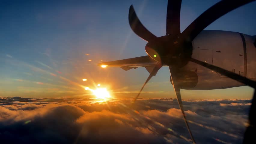 Rotating propeller of an airplane flying against the backdrop of the setting sun above the clouds