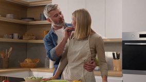 Caucasian married middle-aged couple adult husband and wife cook cuddle at home lovely man feeding beloved woman cucumber slice love happy family cooking salad healthy food at kitchen hugging cuddling - Powered by Shutterstock - Get 15% off with code: PIKWIZARD15