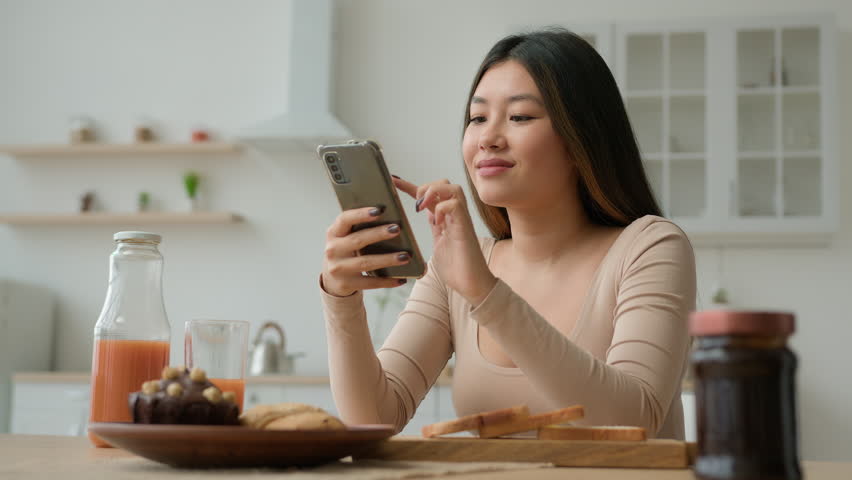 Asian woman in kitchen use smartphone mobile phone application surfing internet. Multiracial korean girl make order food delivery buy grocery in online supermarket search cooking recipe on cellphone Royalty-Free Stock Footage #1103200287