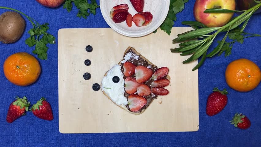Creative kids breakfast, fish made of chocolate bread spread, strawberries and blueberries moving on the wooden board. Stop motion. High quality 4k footage Royalty-Free Stock Footage #1103214575