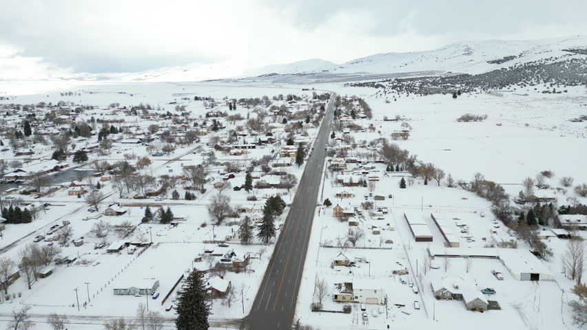 Aerial-Flying over main street-Small mountain valley town under a blanket of new snow - Main street is clear of snow with traffic flowing.