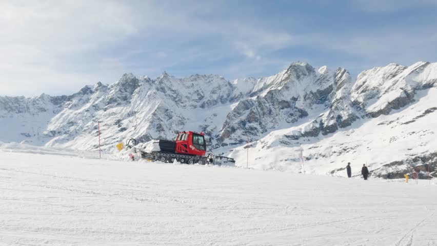Wide shot of snow plow drive on a slope in Cervinia ski resort with mountain range in background