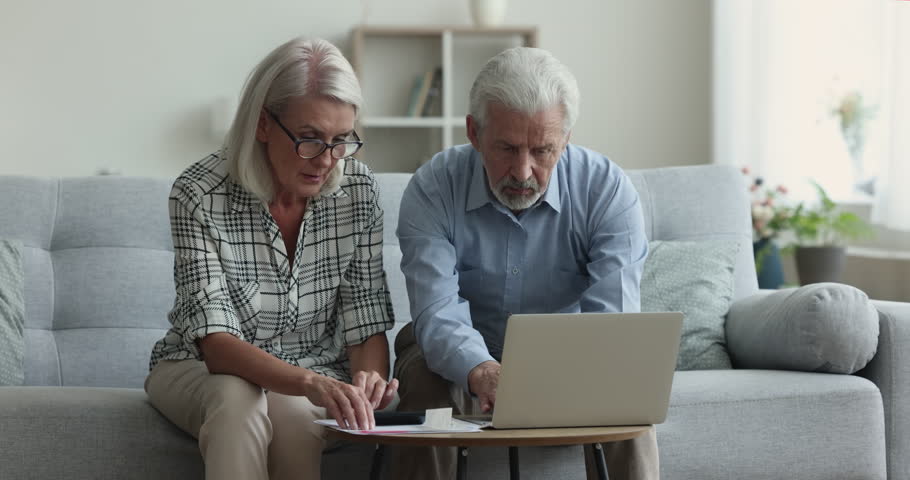 Serious retired couple sit on sofa, count monthly expenses for rent, mortgage, or insurance, manage family budget, feel stressed by lack of money, having financial difficulties, bank debt, overspend Royalty-Free Stock Footage #1103218525