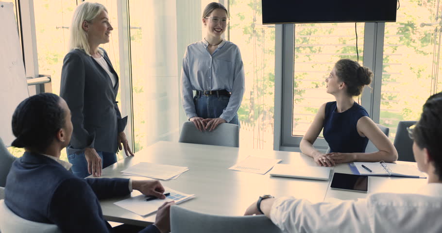 Mature female boss expressing recognition to young employee woman, speaking, hugging with support, gratitude, joining applause of colleagues on office corporate meeting Royalty-Free Stock Footage #1103218637