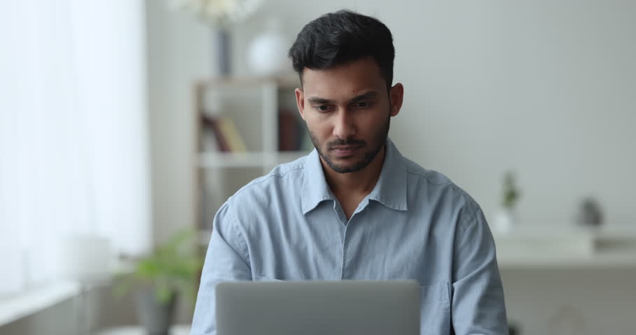 Millennial bearded Indian businessman working from home using laptop, staring at device screen looking pensive and thoughtful, search solution, prepare report or research, doing freelance job on-line Royalty-Free Stock Footage #1103218659