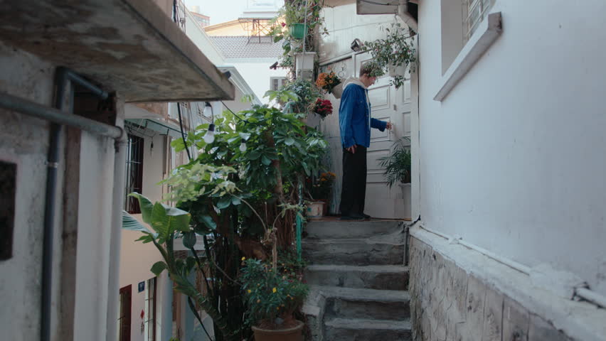 Young woman leaving the house, going downstairs and walking along narrow street in old town. Full shot