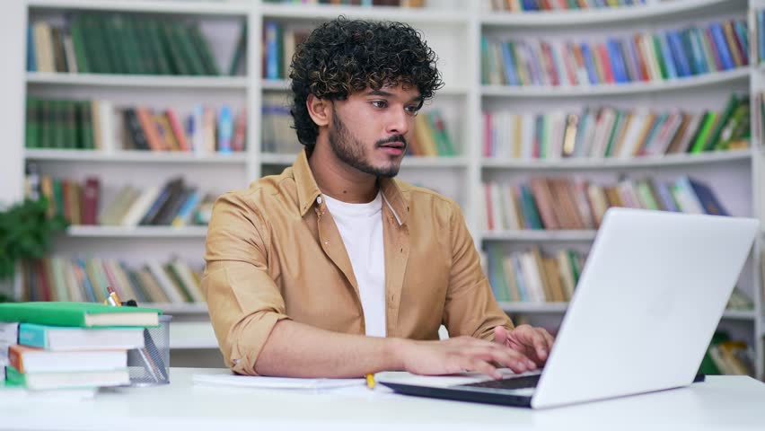 Young student on online e-learning taking notes or video calling remote teacher using laptop computer in campus library space. Handsome male applicant is preparing for university exams in classroom Royalty-Free Stock Footage #1103224425