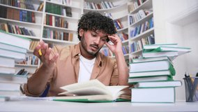 Tired student studying by reading books, taking notes in campus library space. Exhausted male learning on examination period at the university. Overworked applicant is preparing for the entrance exams - Powered by Shutterstock - Get 15% off with code: PIKWIZARD15