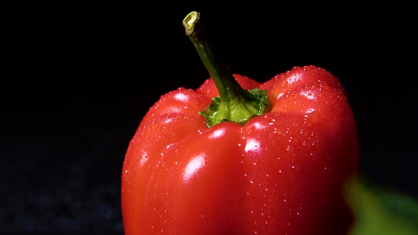 Close-up of fresh organic red bell pepper with green tail covered with water drops on a black table on a dark background. Royalty-Free Stock Footage #1103228313