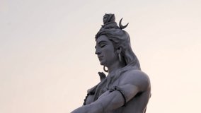 hindu god lord shiva statue in meditation posture with flat sky at evening from low angle video is taken at parmarth niketan rishikesh uttrakhand india on Mar 15 2022.