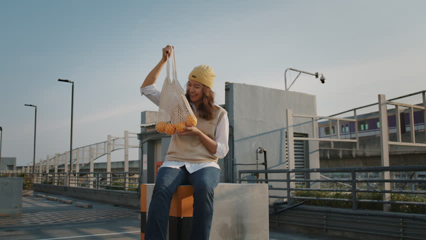 Young Gen Z woman asia people smile look at camera showing carry fruit in eco friendly care reuse mesh bag. Go green urban city life net zero waste Save the earth no plastic garbage free reduce trash.