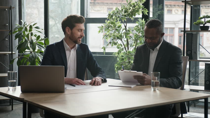 Two diverse businessmen at office meeting shake hands after successful business contract agreement. African businessman signing paper document offer Caucasian man salesman handshake client customer Royalty-Free Stock Footage #1103233133