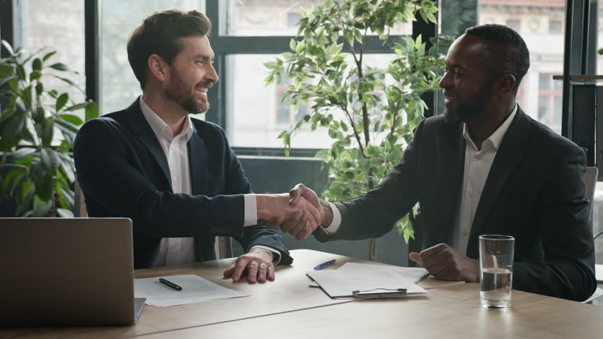 Two diverse businessmen at office meeting shake hands after successful business contract agreement. African businessman signing paper document offer Caucasian man salesman handshake client customer Royalty-Free Stock Footage #1103233133