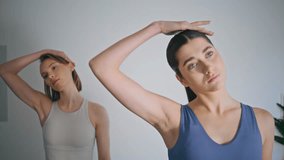 Athletes couple stretching neck practicing yoga indoors. Closeup mindful girls warming head up using right hand at white home. Serene relaxed women training cervical spine joints exercising together  - Powered by Shutterstock - Get 15% off with code: PIKWIZARD15