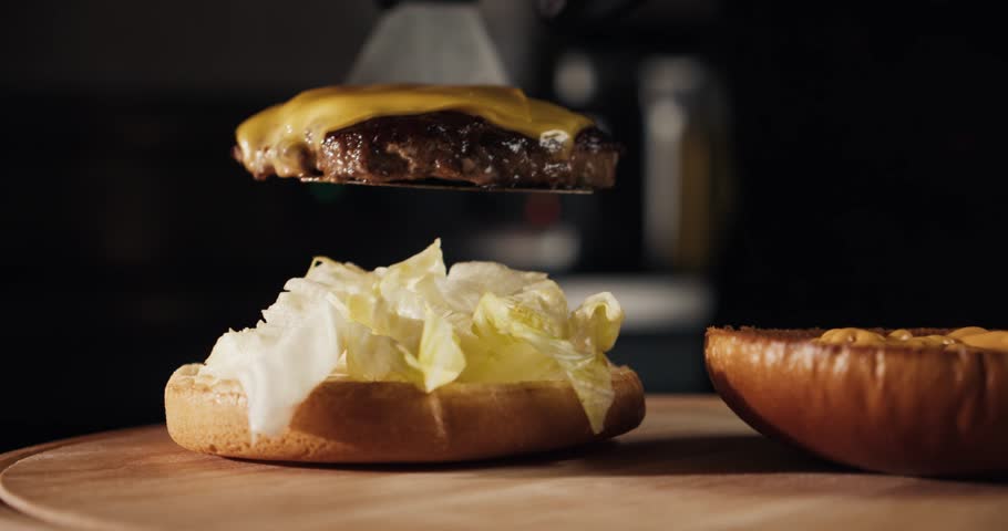a chef in black gloves puts a beef patty with melted cheese on top of a burger  Royalty-Free Stock Footage #1103245297