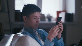 Teen Boy Enjoying Digital Leisure Activities: Chatting with Friends and Playing Games on Phone While Relaxing by the Window