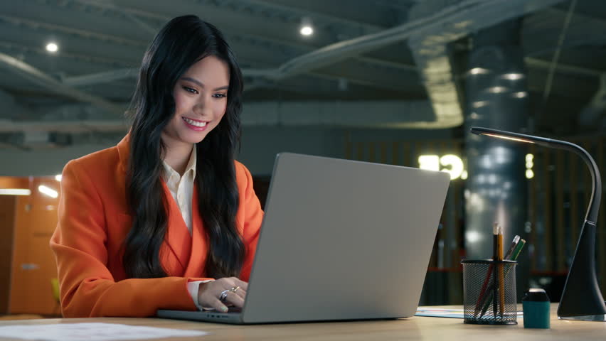 Confident positive asian businesswoman with pretty smile looking at laptop screen, slow motion. Happy cheerful startup entrepreneur typing in email on laptop, sitting at desk at open space loft office Royalty-Free Stock Footage #1103258365