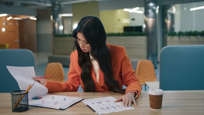 Tired stressed girl looking at reports tables, grabs her head with hand while working hard at late night at empty office. Exhausted asian business woman reviewing documents on desk with paperwork 4K Royalty-Free Stock Footage #1103258379
