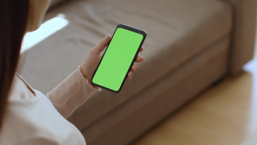 Digital tv app. Over shoulder view of young lady watching show on smartphone with green chroma key screen, resting st home, slow motion, empty space for mockup Royalty-Free Stock Footage #1103258811