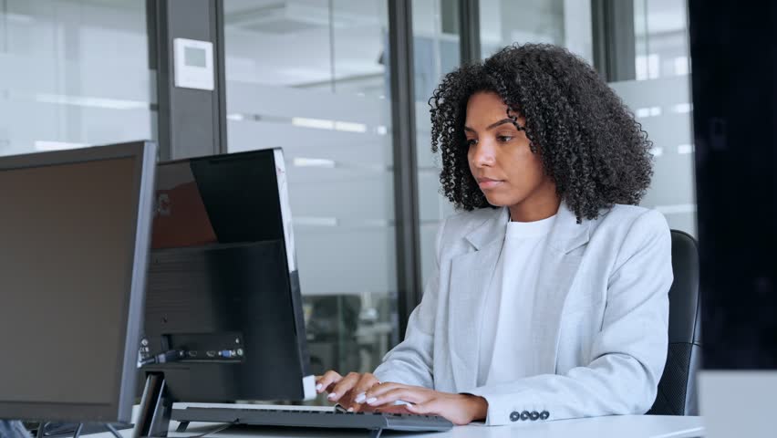 Middle age business woman working, browsing, and typing on touchscreen pc laptop. African American young female businesswoman, successful entrepreneur using app gadget sitting at work place in office. Royalty-Free Stock Footage #1103259869