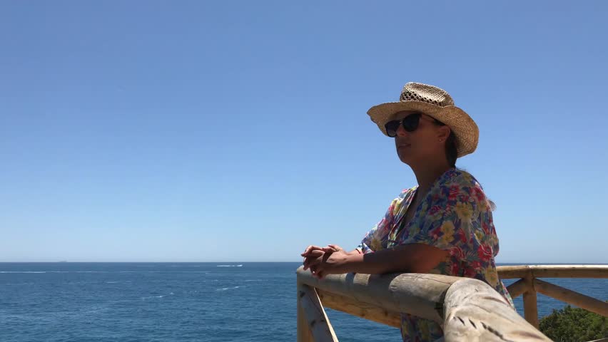 Young woman in hat and sunglasses from a viewpoint looking the ocean