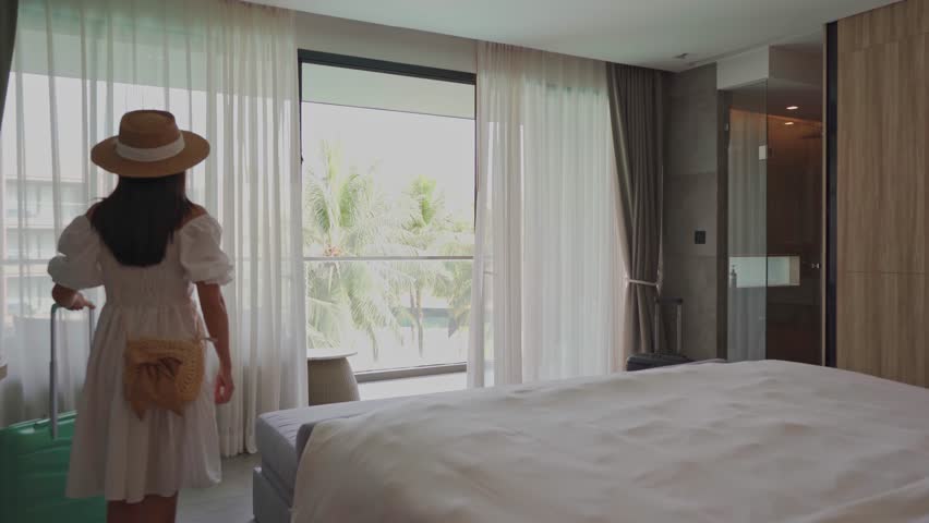 Young woman traveler opening the curtains and looking at the view from the window of a hotel room while on summer vacation, Travel lifestyle concept Royalty-Free Stock Footage #1103267049