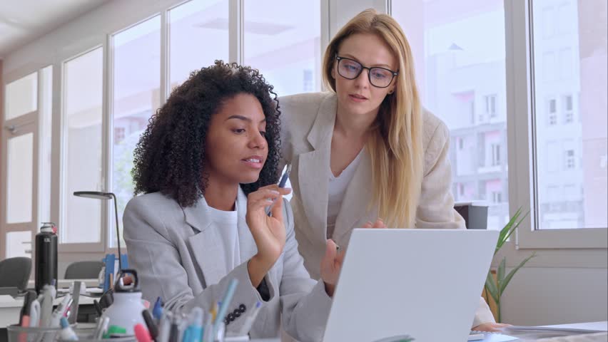 Two businesswoman working together using laptop pc, sitting at table and discussing a project. Small creative diversity team of African American and blond females executives meeting work in office. Royalty-Free Stock Footage #1103268527