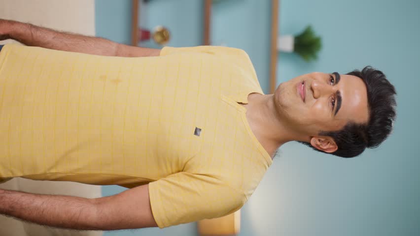 vertical shot of Happy smiling indian young man standing with arms crossedby looking camera at home - concept of successful, confident and relaxed.