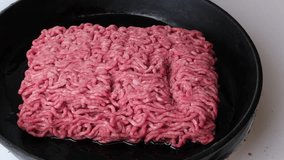 Close video of wooden spoon breaking apart a pound of ground beef or hamburger meat in a hot frying pan. 