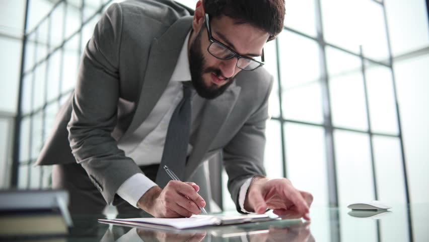 Businessman leaning over office desk signing a contract with superficial attention to signature