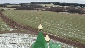 Aerial view of a church with green roof and golden domes. Clip. Church surrounded by green farm fields in early spring.