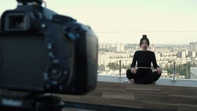 Woman beauty blogger in black clothes is talking, sits cross-legged, participating yoga in video conference, remotely negotiating with clients. Video tutorial for work or study on rooftop terrace