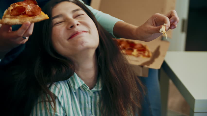 Multiracial happy young people eating pizza on sofa and laugh, cheerful students enjoying meal dining sitting together, diverse hungry friends sharing lunch at meeting sharing pizza. Everybody