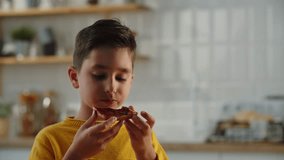 A smiling boy in a yellow sweater is eating a sandwich with raspberry jam. The young man was hungry and decided to have a sandwich to eat.