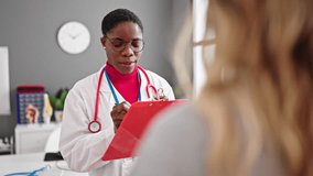 African american woman doctor writing medical report speaking with patient at clinic - Powered by Shutterstock - Get 15% off with code: PIKWIZARD15