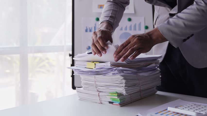 work from office A businessman works a bunch of paper files to find information on his desk at home. business report pile of unfinished documents
