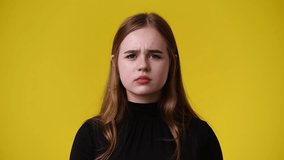 4k video of cute girl with negative facial expression on yellow background.