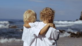 Rear view of two children hugging each other by shoulders on seashore or ocean. Two children on shore hug and enjoy the view eating lollipops. Little caucasian kids get new impression from trip to sea - Powered by Shutterstock - Get 15% off with code: PIKWIZARD15