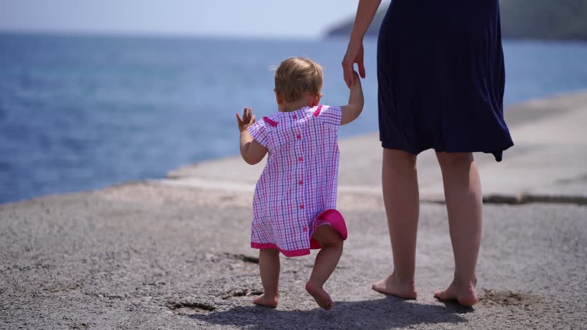 Mom and a little girl walk barefoot along the pier and look at the sea. Cropped