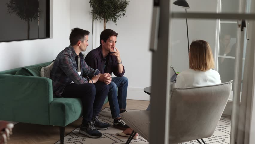 gay male couple on successful visit to psychologist, married couple sitting together on sofa after good family therapy session, satisfied clients, help spouse to solve problem Royalty-Free Stock Footage #1103310519