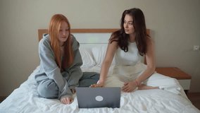Two teenage girls having break at home using laptop, watch video film, social media, clip, reel. Young women talking, gossip, chitchat, having fun.