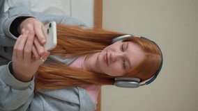 Teenage girl headphones using smartphone at home on bed. Young woman listen to music online podcast watch video with gadget, online chatting messaging with friends Internet technology, communication